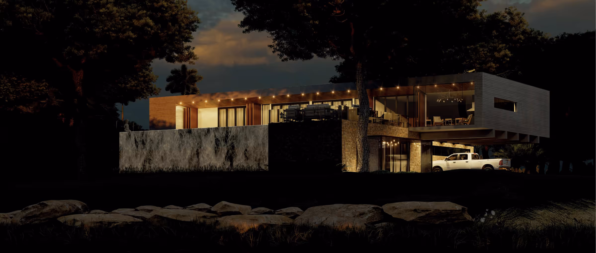 Cena noturna: a casa iluminada vista de longe, com pedras em primeiro plano